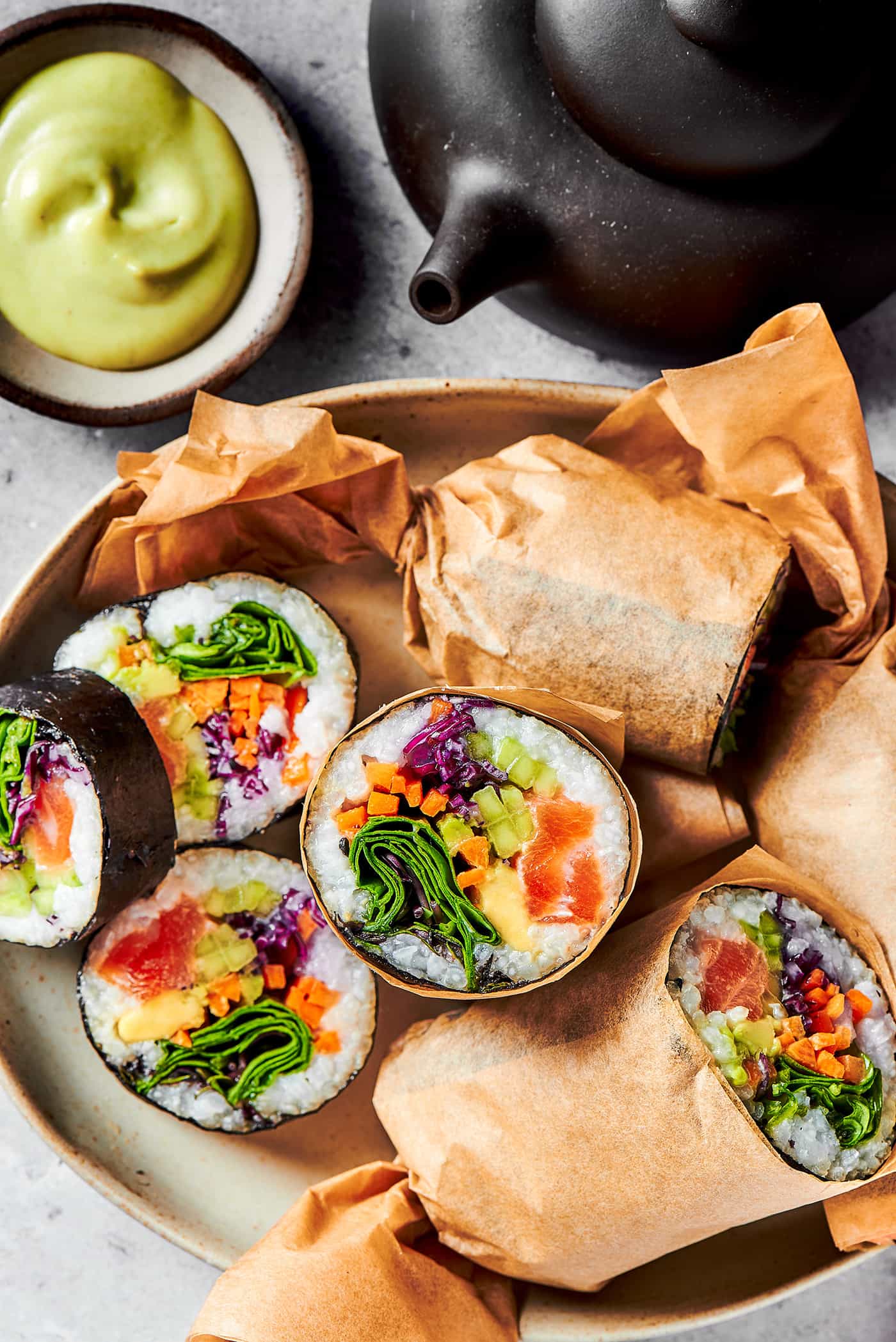 sushi burritos cut in half, on a platter with wasabi dip