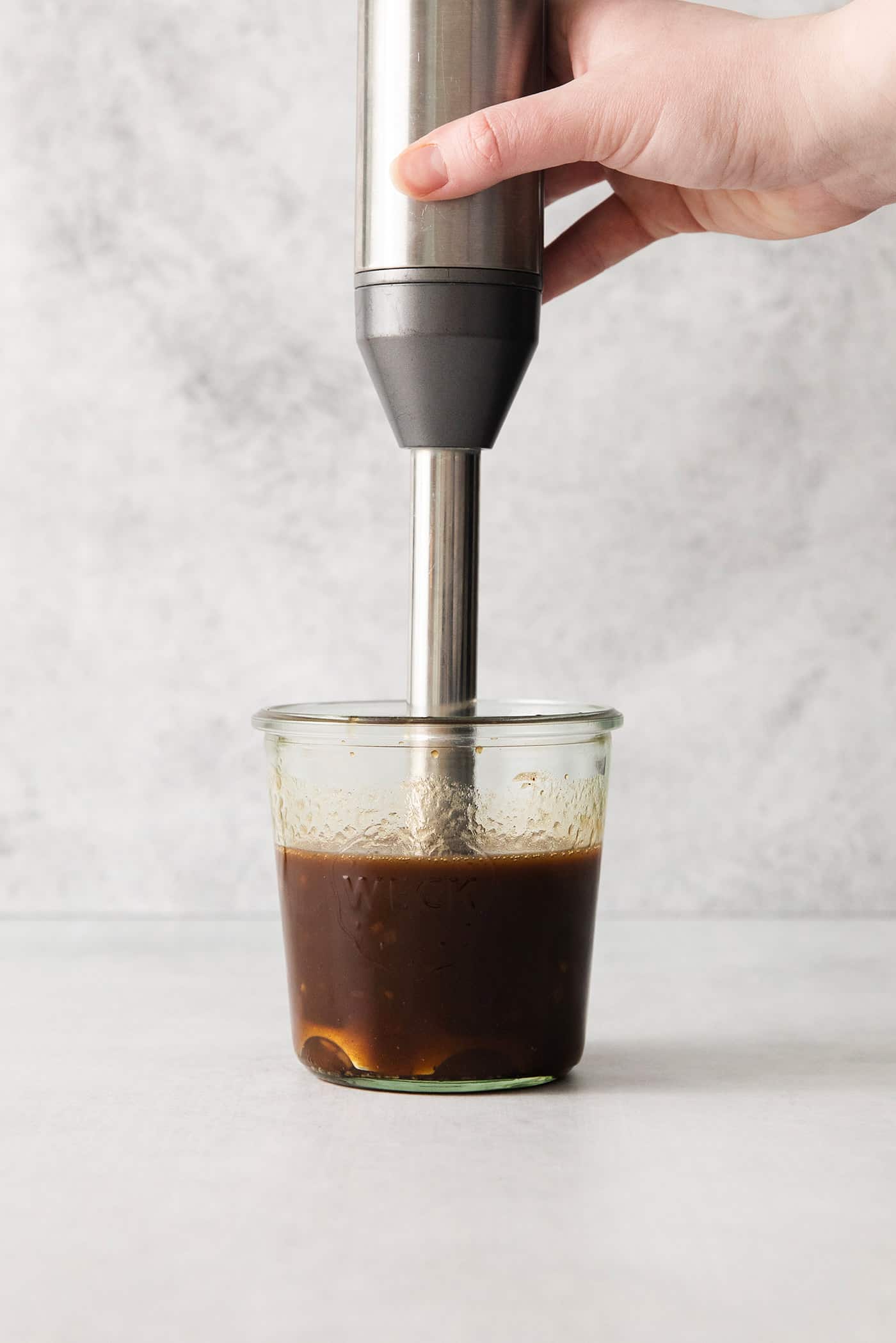 An immersion blender in a jar with balsamic vinegar and olive oil