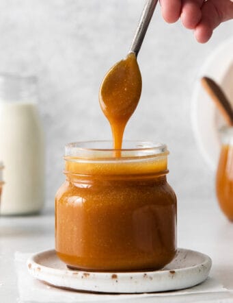 A spoon dripping caramel sauce back into the jar