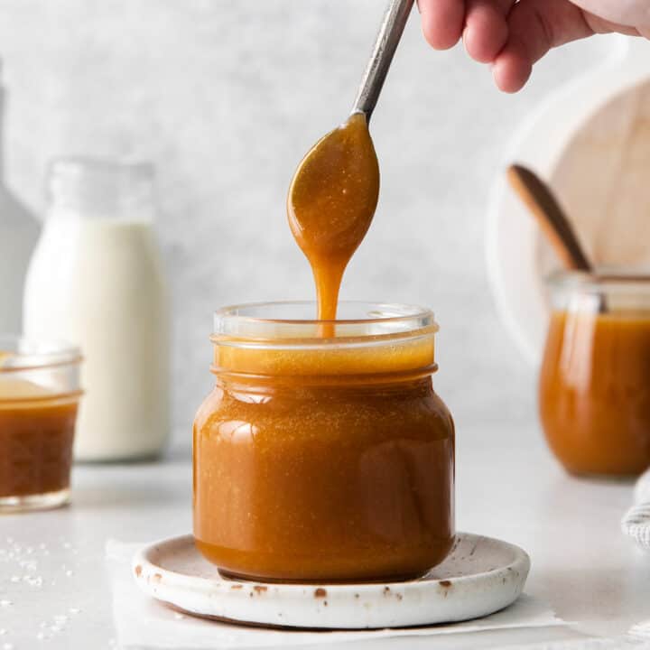 A spoon dripping caramel sauce back into the jar