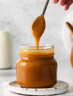 A spoon drizzling caramel syrup back into a jar