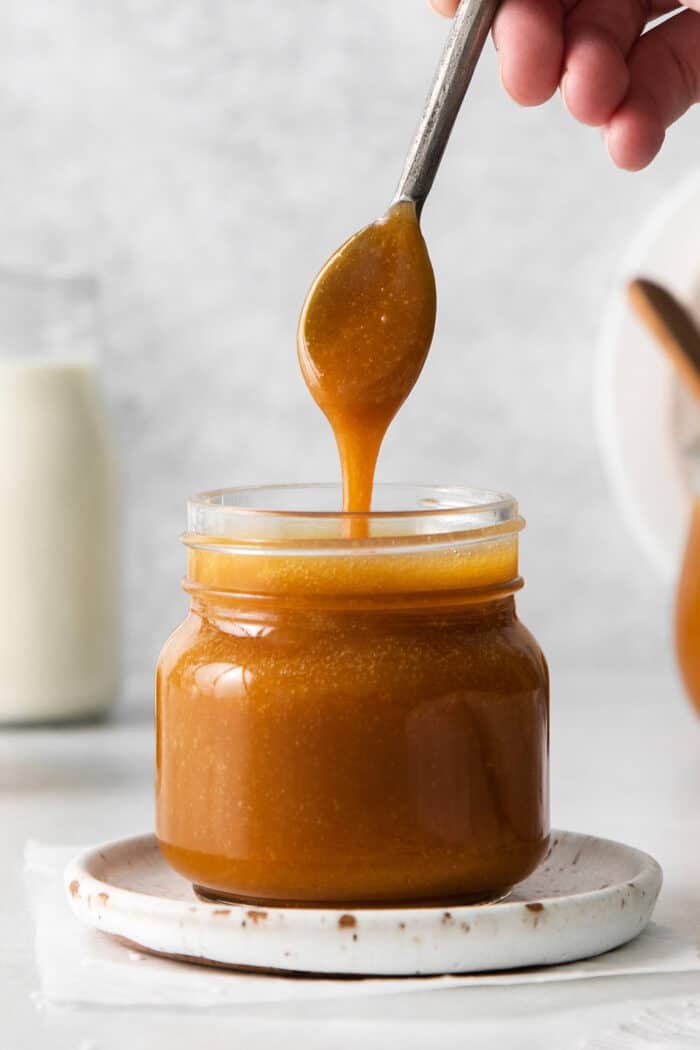 A spoon drizzling caramel syrup back into a jar