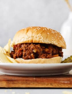 A sloppy joe sandwich on a plate with chips and pickles