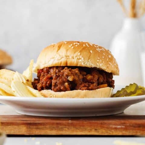 A sloppy joe sandwich on a plate with chips and pickles