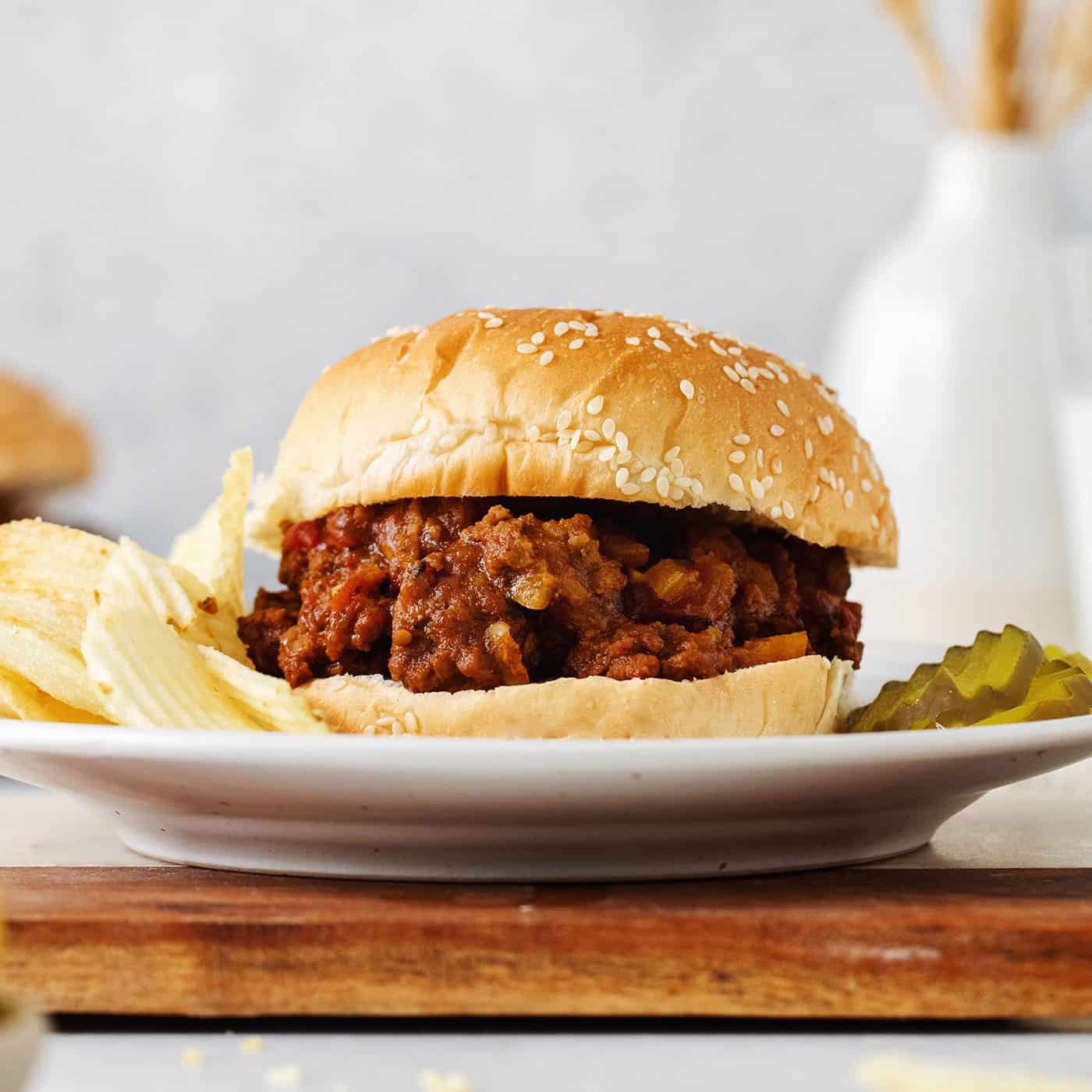 A sloppy joe sandwich on a plate with chips and pickles