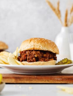 A sloppy joe sandwich on a plate with chips and pickles