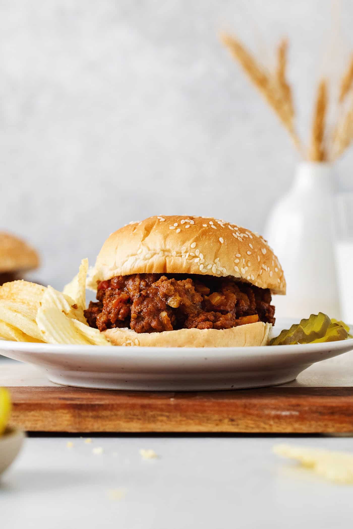 A sloppy joe sandwich on a plate with chips and pickles