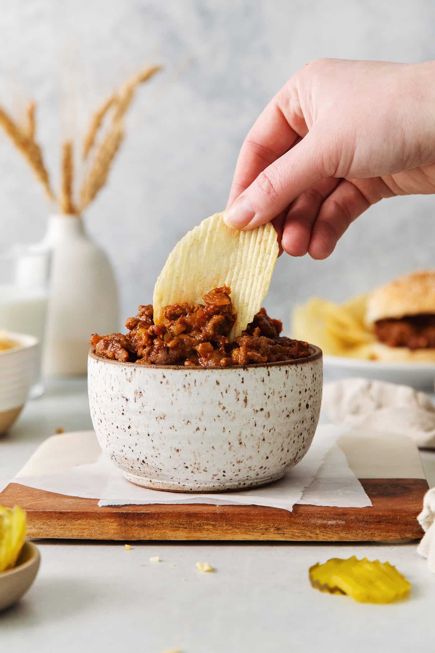 A hand dipping a chip in sloppy joe meat