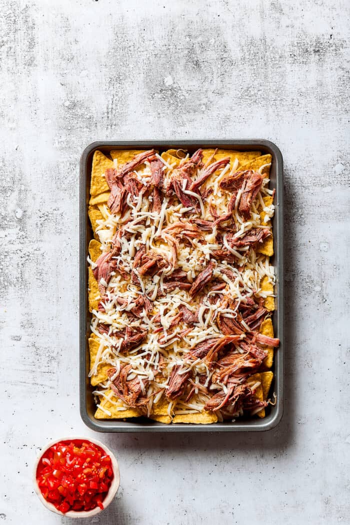 Tortilla chips topped with pulled pork on a baking sheet