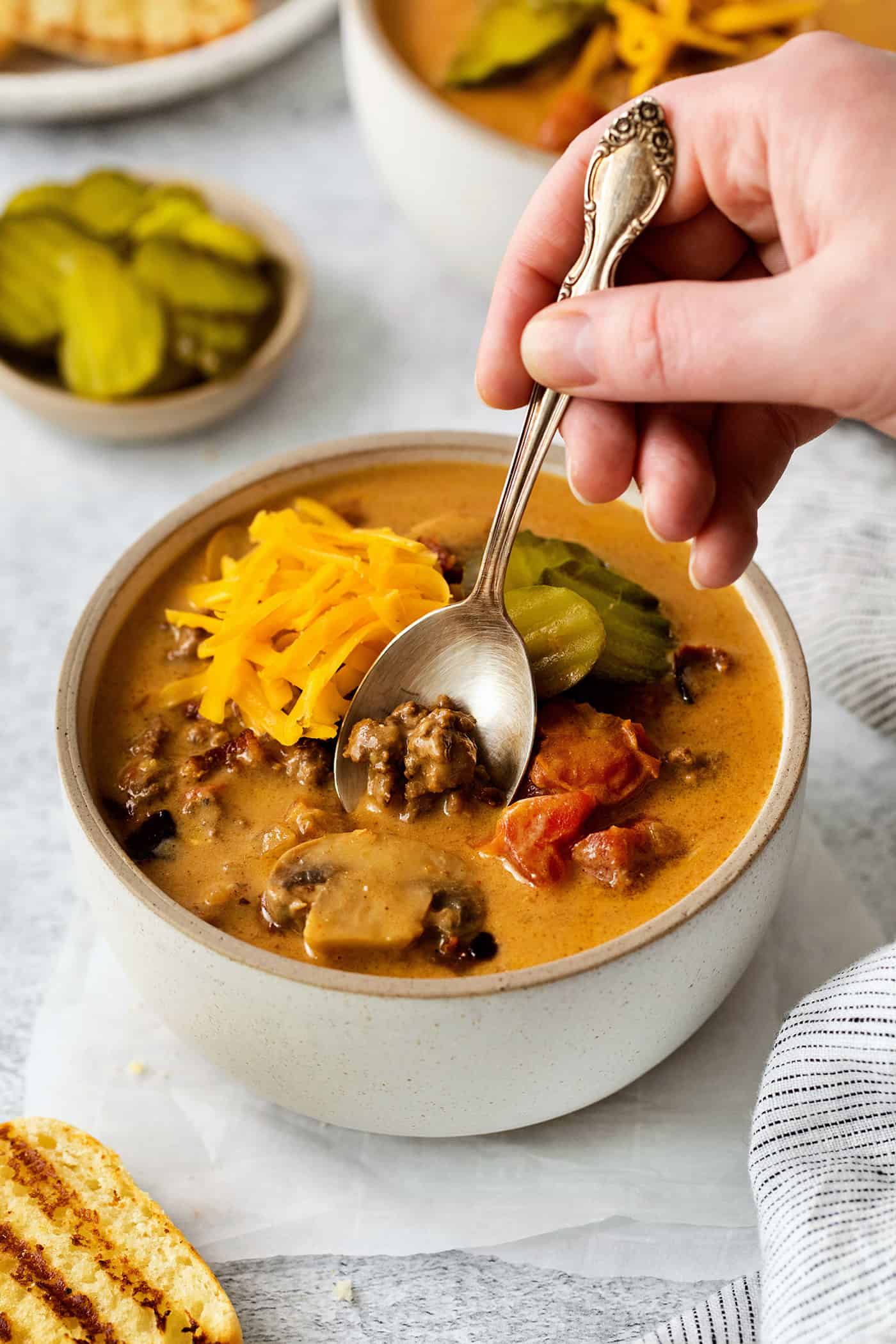 a hand with a spoon, dipping into a bowl of soup