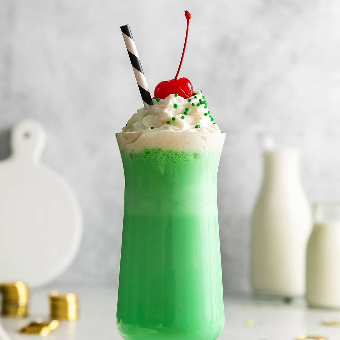 a tall glass with a green mint shake that is topped with whipped cream and a cherry