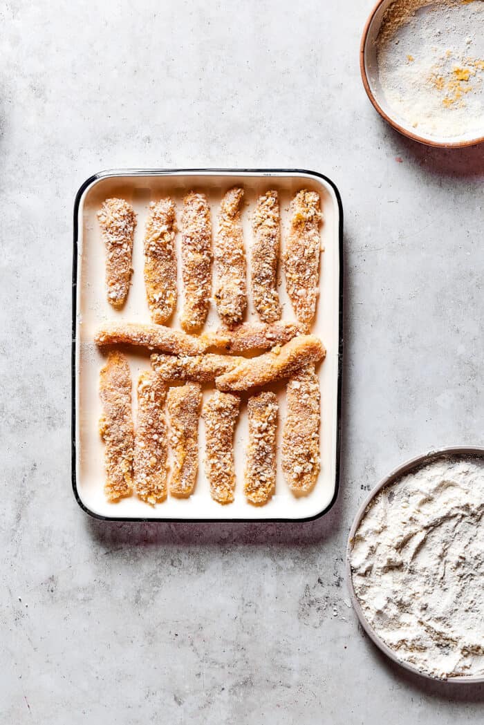 strips of chicken coated in breading, on a white pan