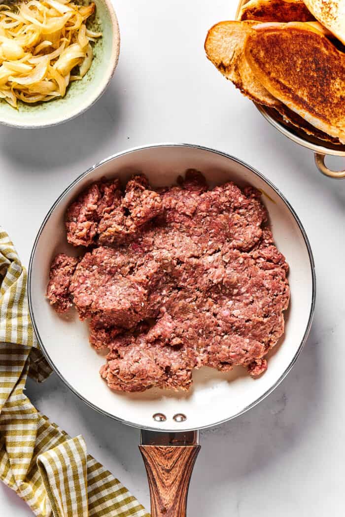 a pound of seasoned ground beef patty cooking in a skillet
