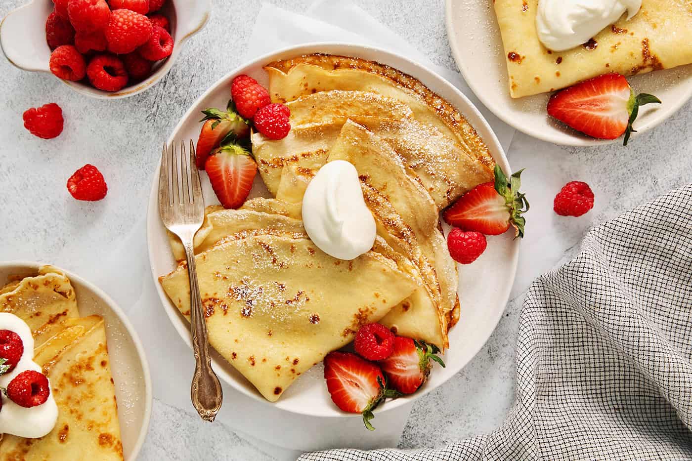 A plate of French crepes topped with fruit on a table.