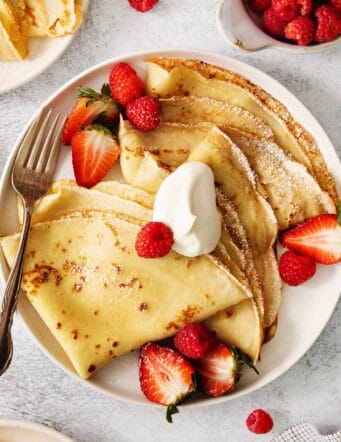 A plate of French crepes topped with fruit on a table.