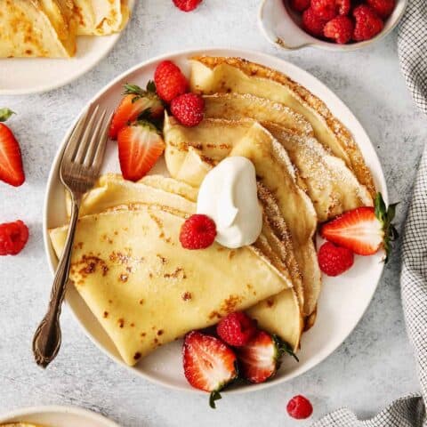 A plate of French crepes topped with fruit on a table.