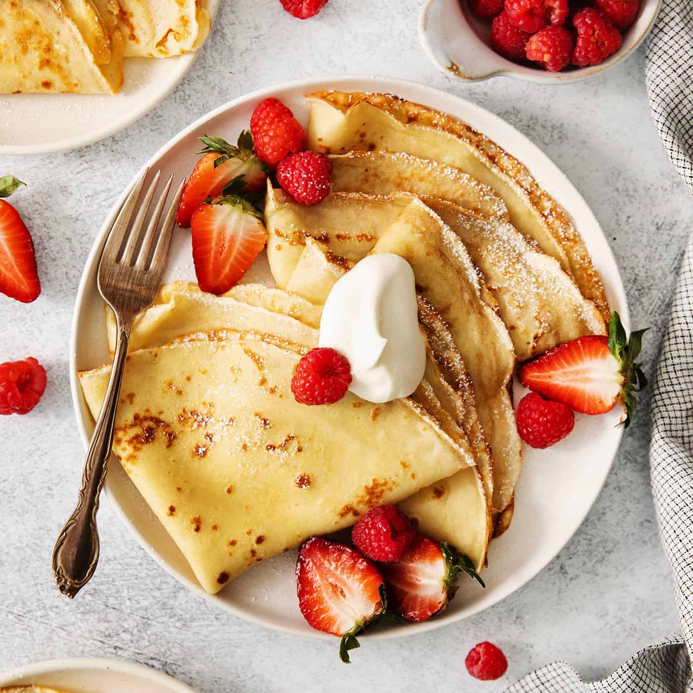 A plate of French crepes topped with fruit on a table.