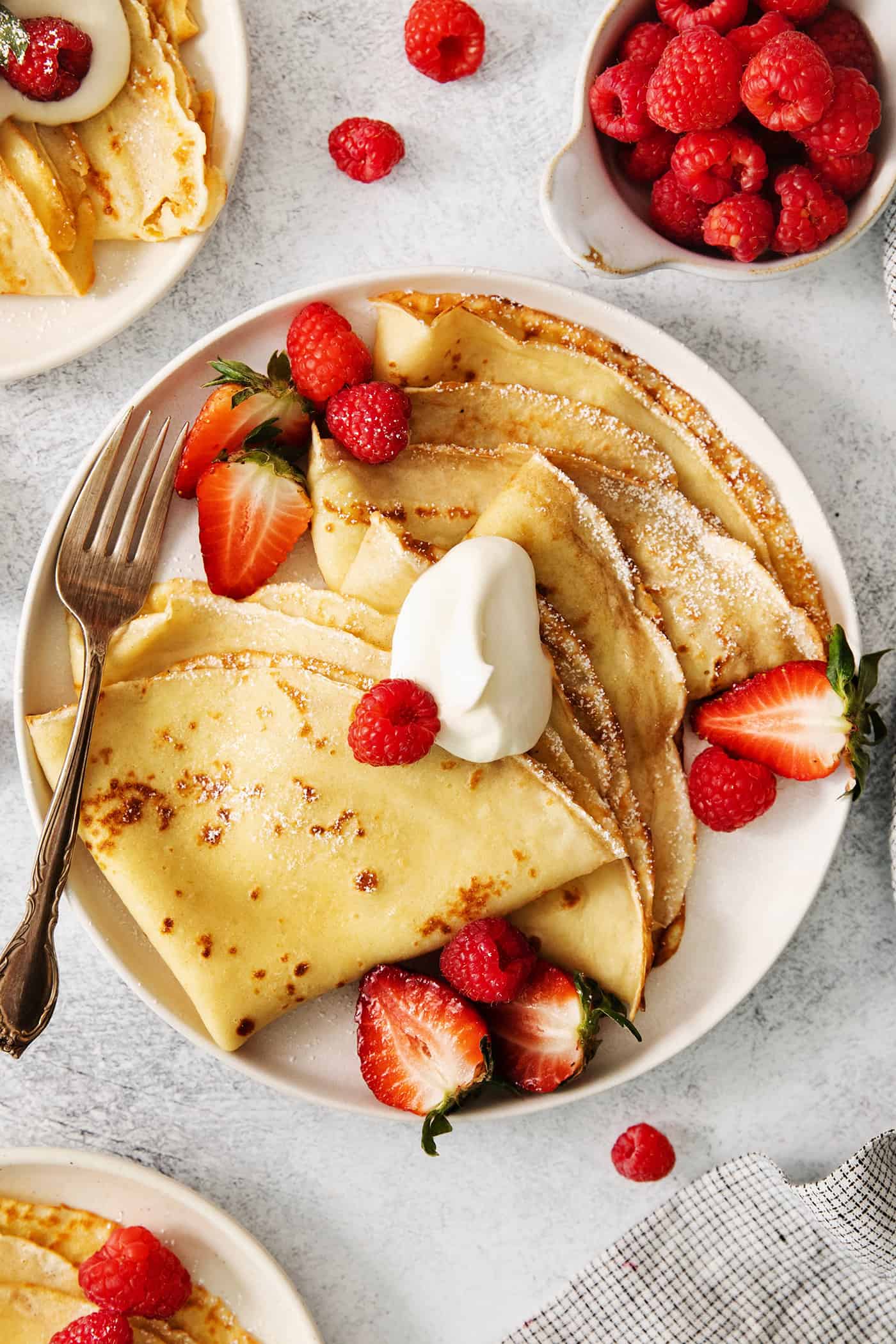 A plate of French crepes topped with fruit on a table.