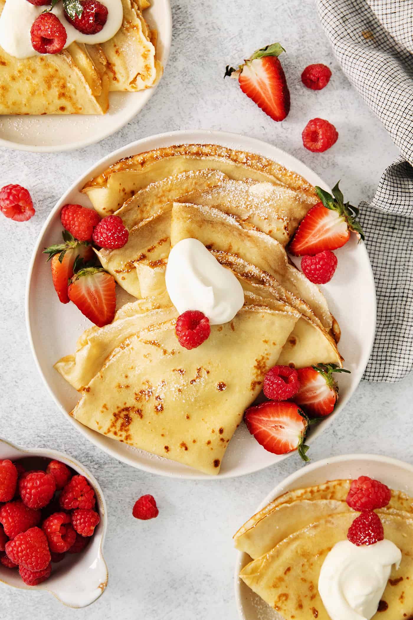 A plate of French crepes topped with strawberries on a table.