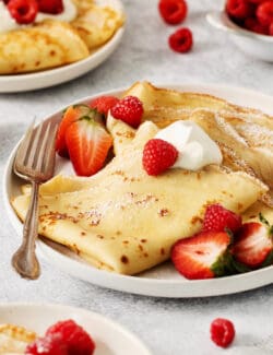 A plate of French crepes topped with strawberries on a table.