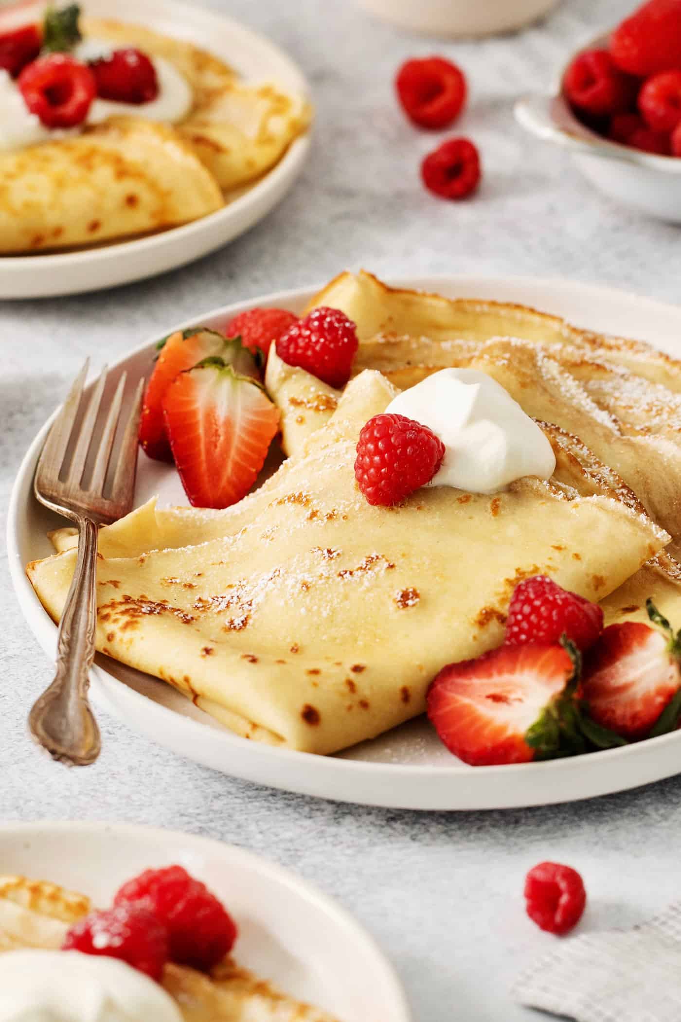 A plate of French crepes topped with strawberries on a table.