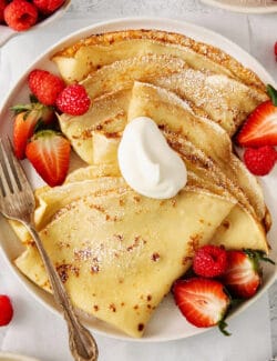 A plate of French crepes topped with strawberries on a table.