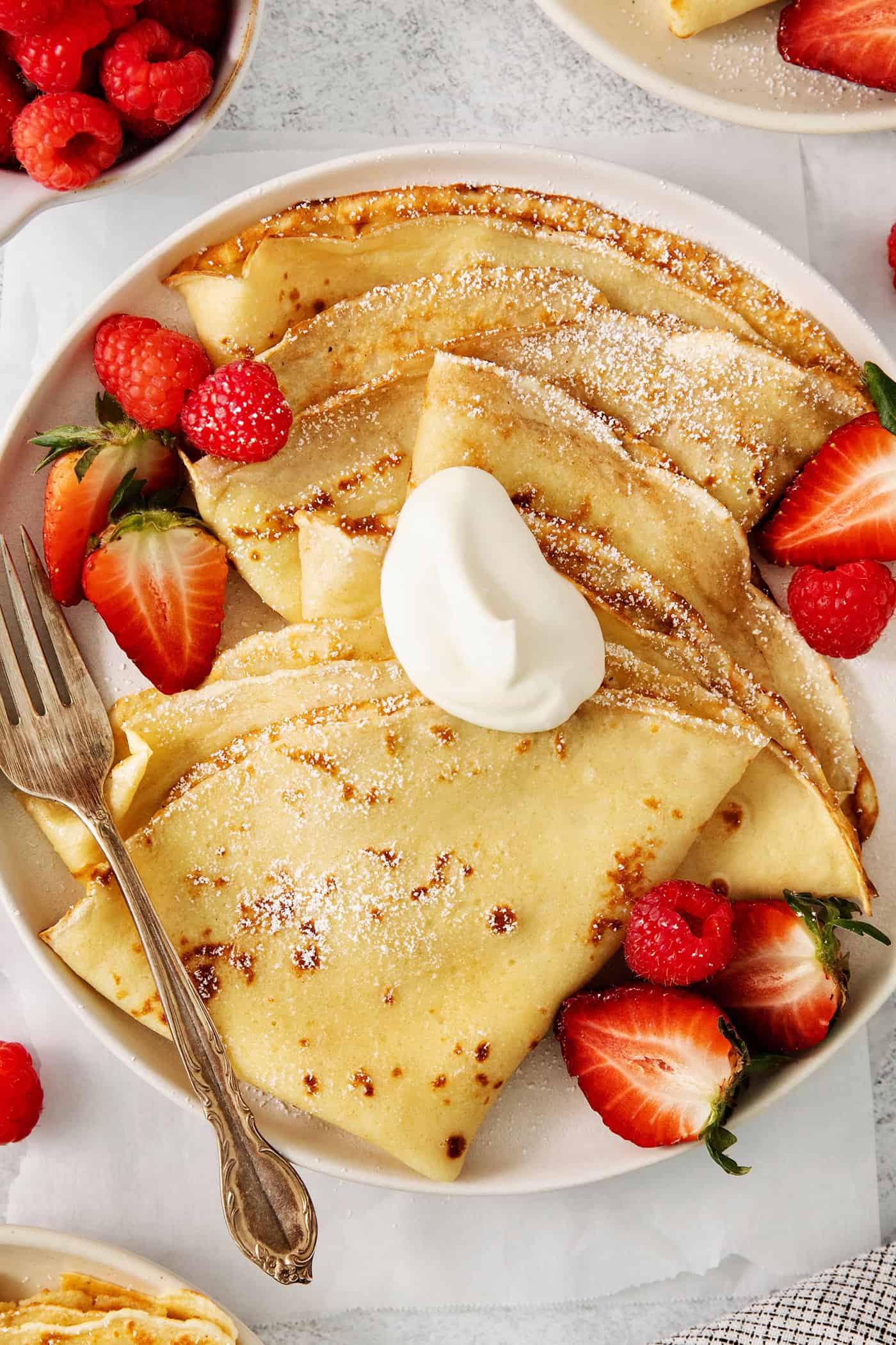 A plate of French crepes topped with strawberries on a table.