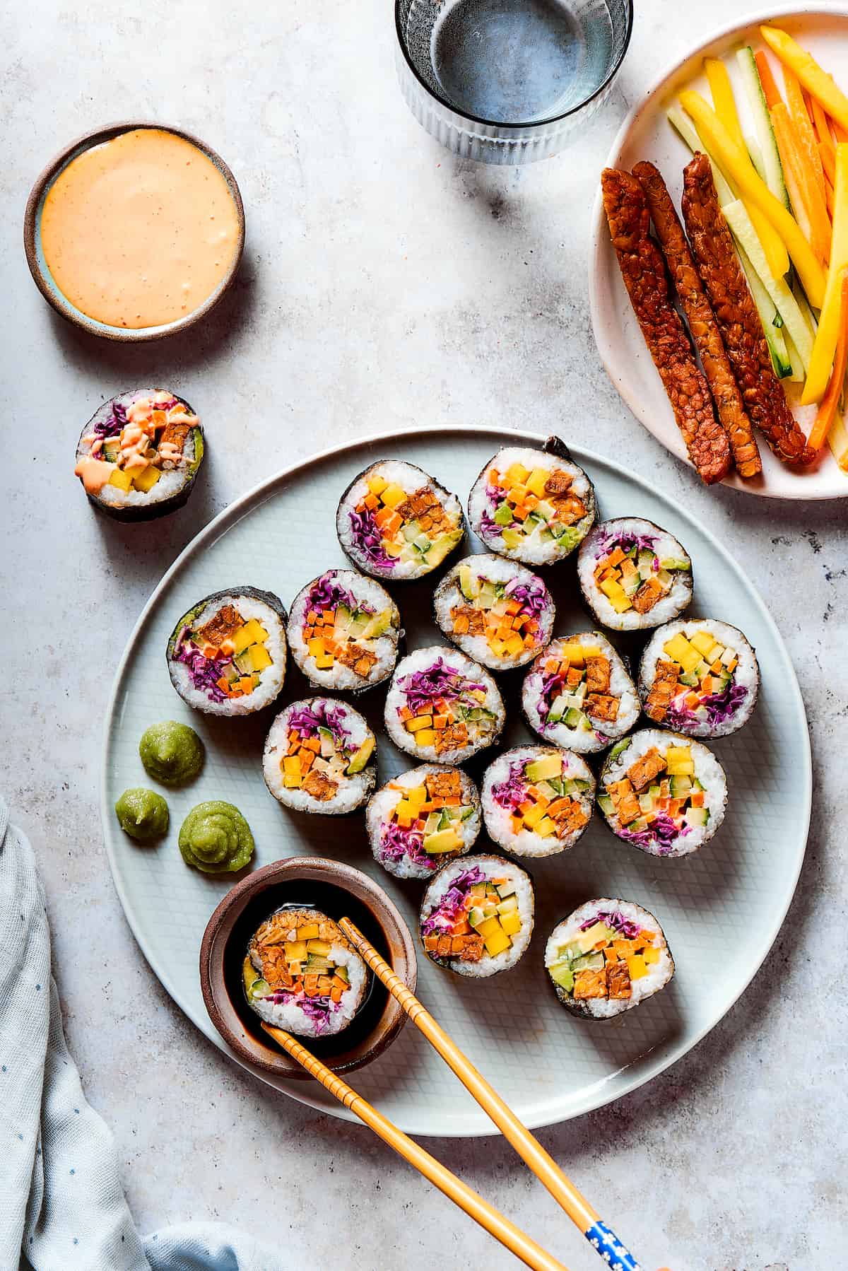 Overhead view of a plate of vegan sushi with chopsticks dipping on into soy sauce