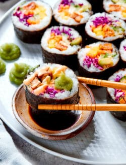 Chopsticks dipping a piece of sushi into soy sauce