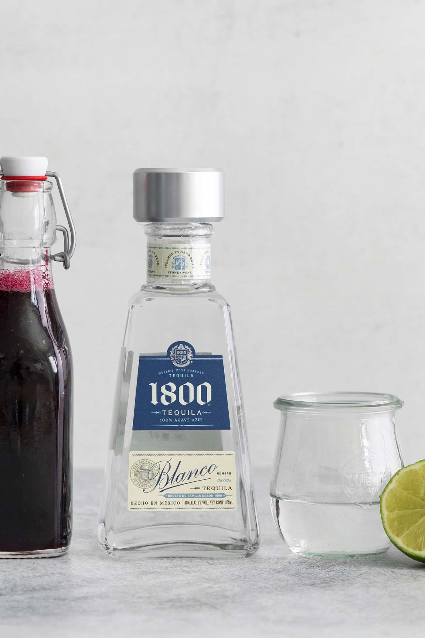 a bottle of 1800 Tequila Blanco, plus blueberry juice and a lime