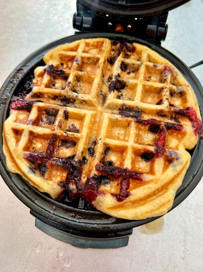 A blueberry waffle cooks on a waffle iron.