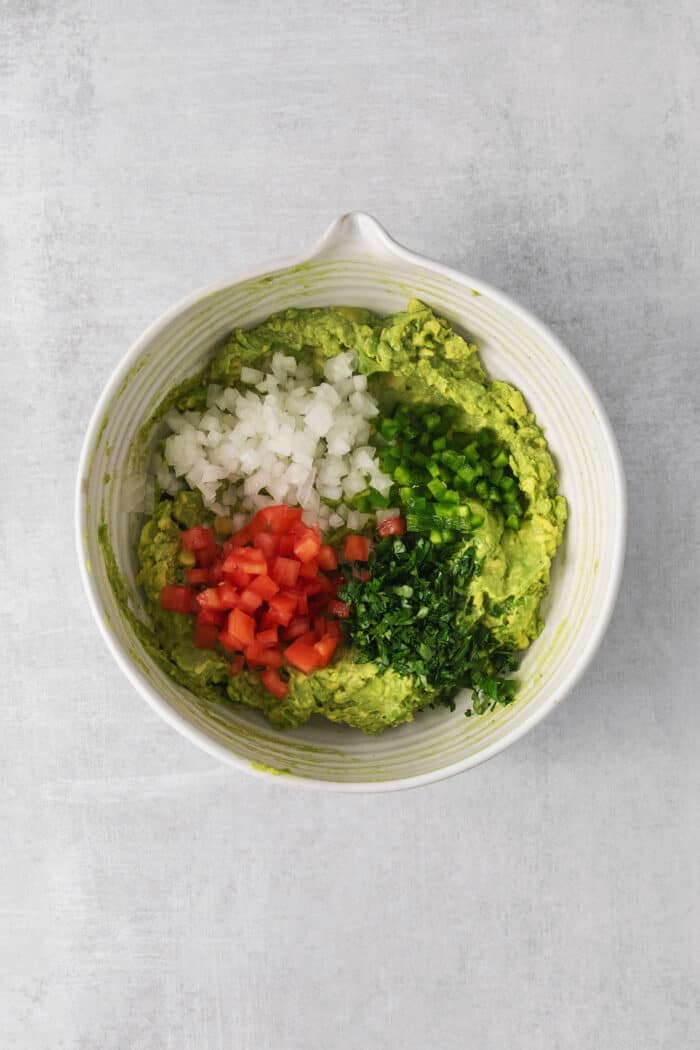 Mashed avocado in a bowl with onion, cilantro, tomatoes, and jalapeno
