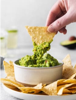A hand dipping a chip into some fresh guacamole