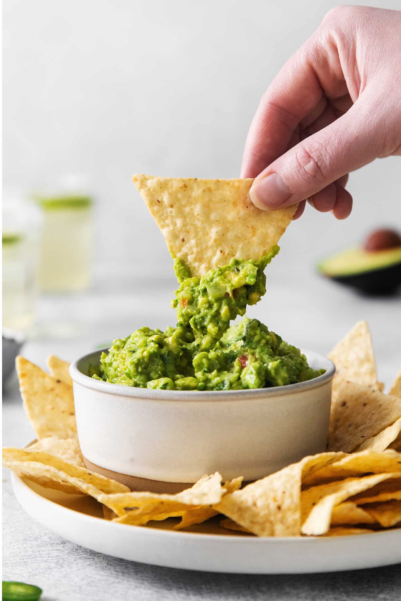 A hand dipping a chip into some fresh guacamole
