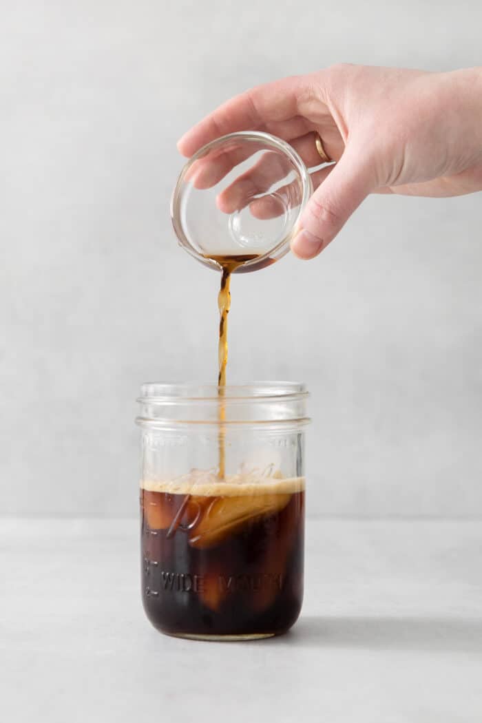 Brown sugar syrup being added to a jar with espresso and ice