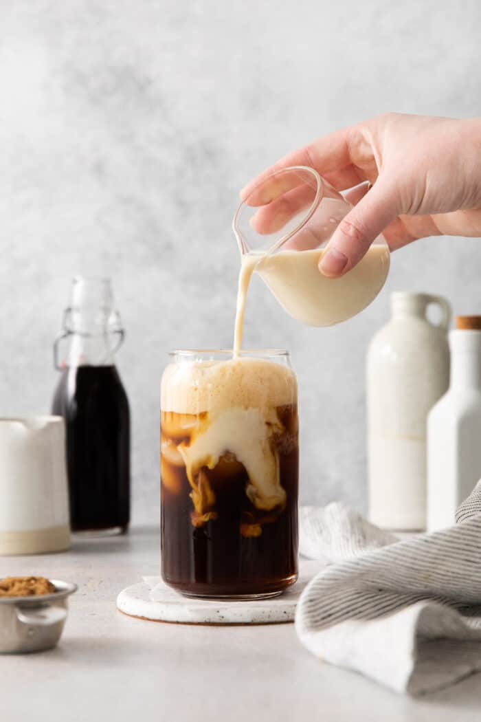 Oatmilk being poured into a glass with espresso