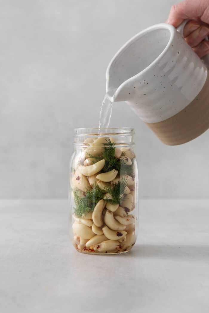 Pickling liquid being poured into a jar of garlic cloves