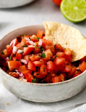 A white bowl of pico de gallo with a tortilla chip