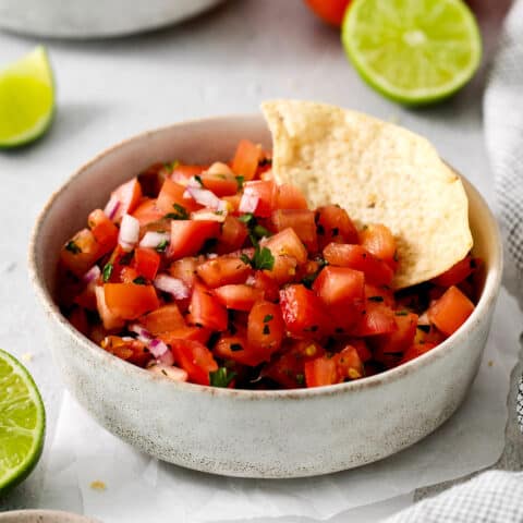 A white bowl of pico de gallo with a tortilla chip