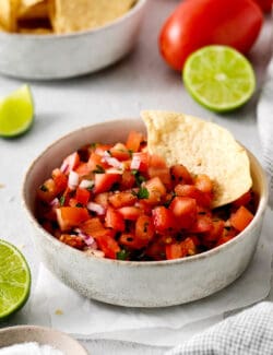 A tortilla chip in a bowl of pico de gallo