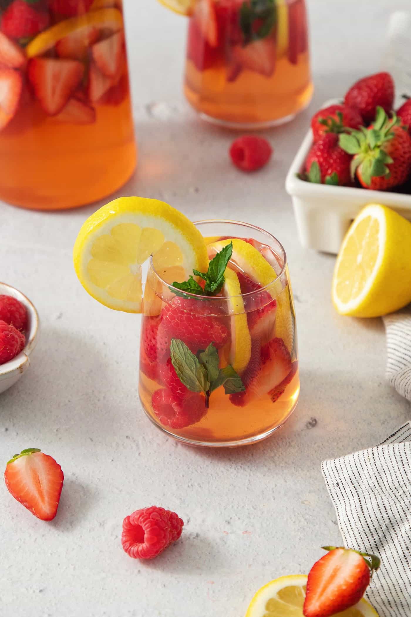 A glass of rose sangria is seen on a table garnished with a lemon.
