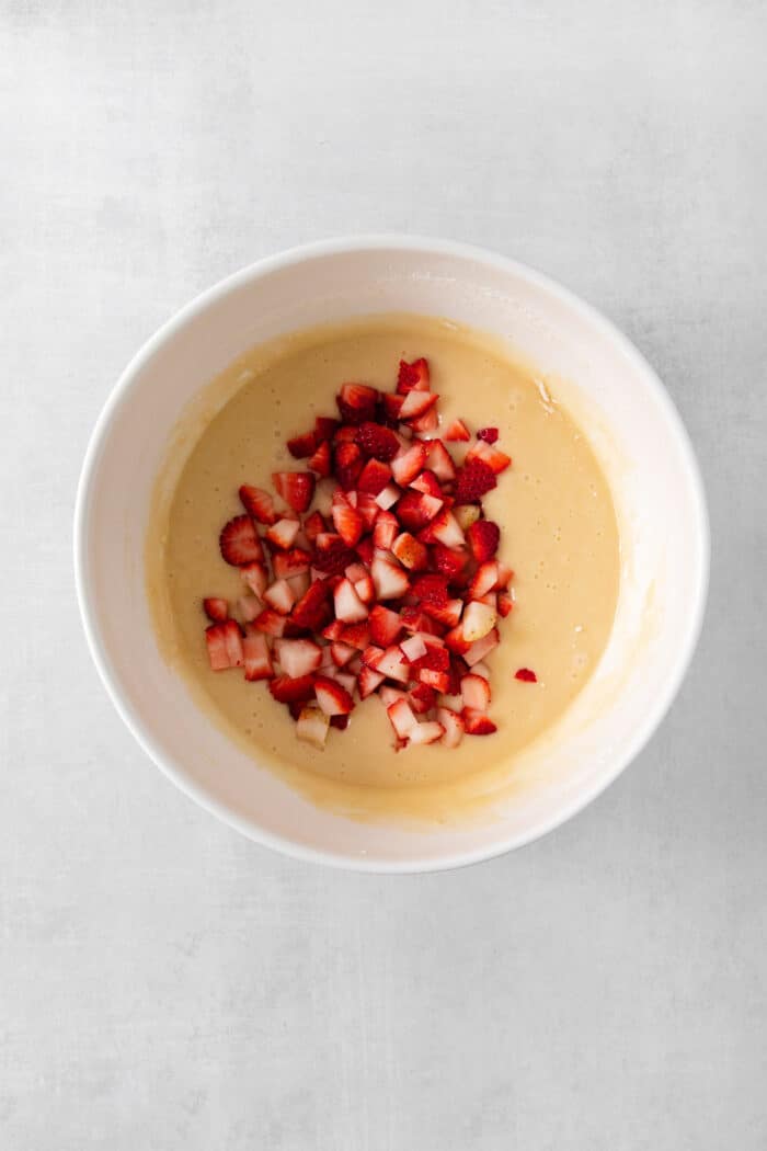 A bowl of cupcake batter is topped with fresh strawberries.