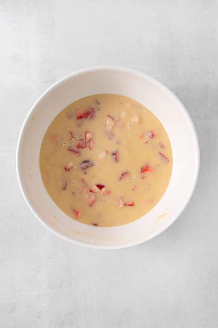 Strawberries are shown in a bowl of cupcake batter.