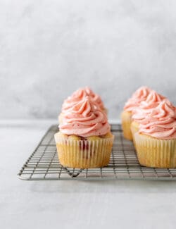 A wire rack with three strawberry cupcakes on it.