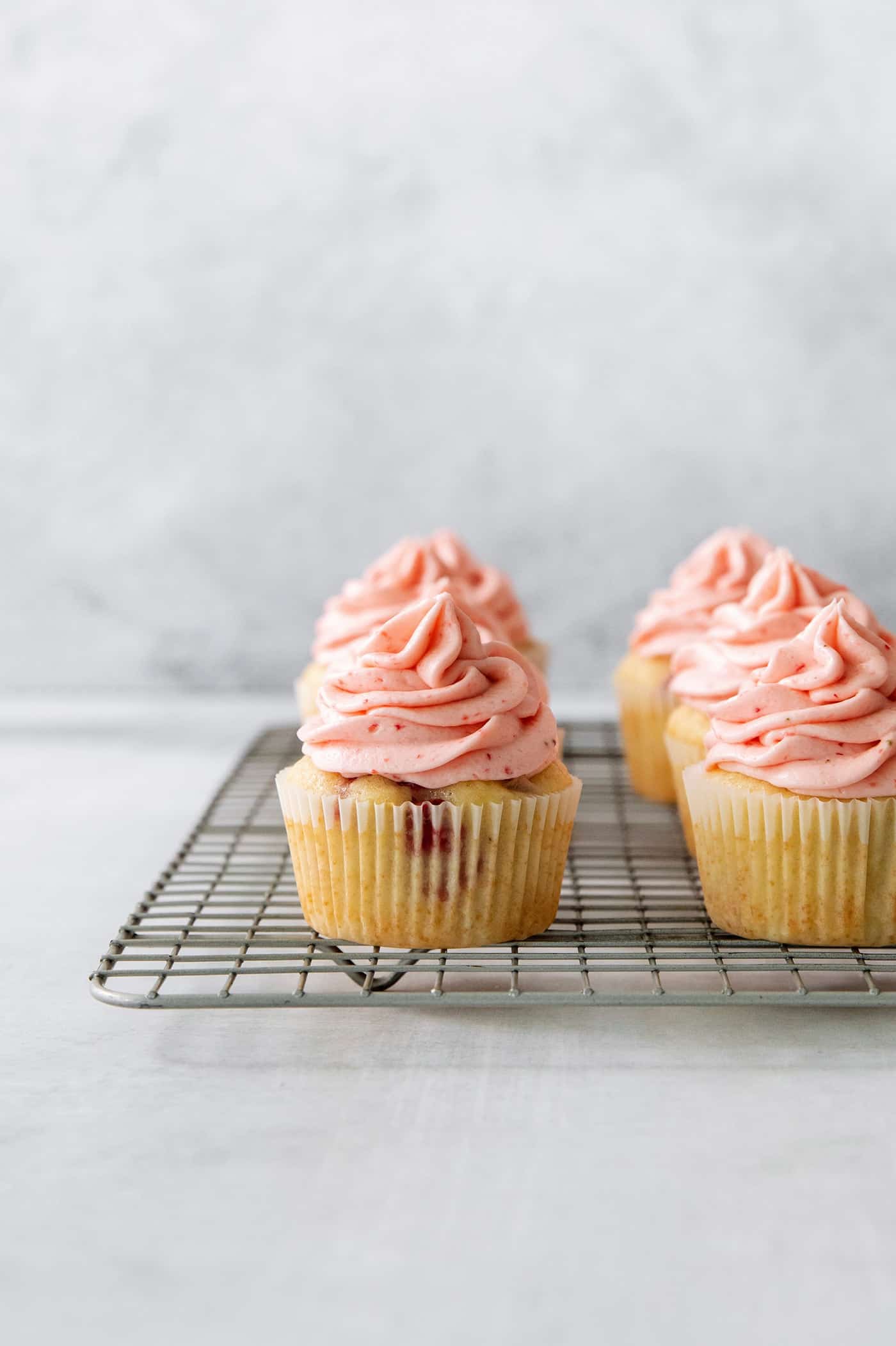 A wire rack with three strawberry cupcakes on it.