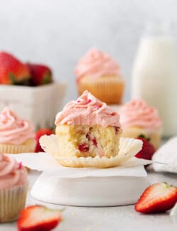 A batch of frosted strawberry cupcakes is shown with one cupcake cut open to show the interior.