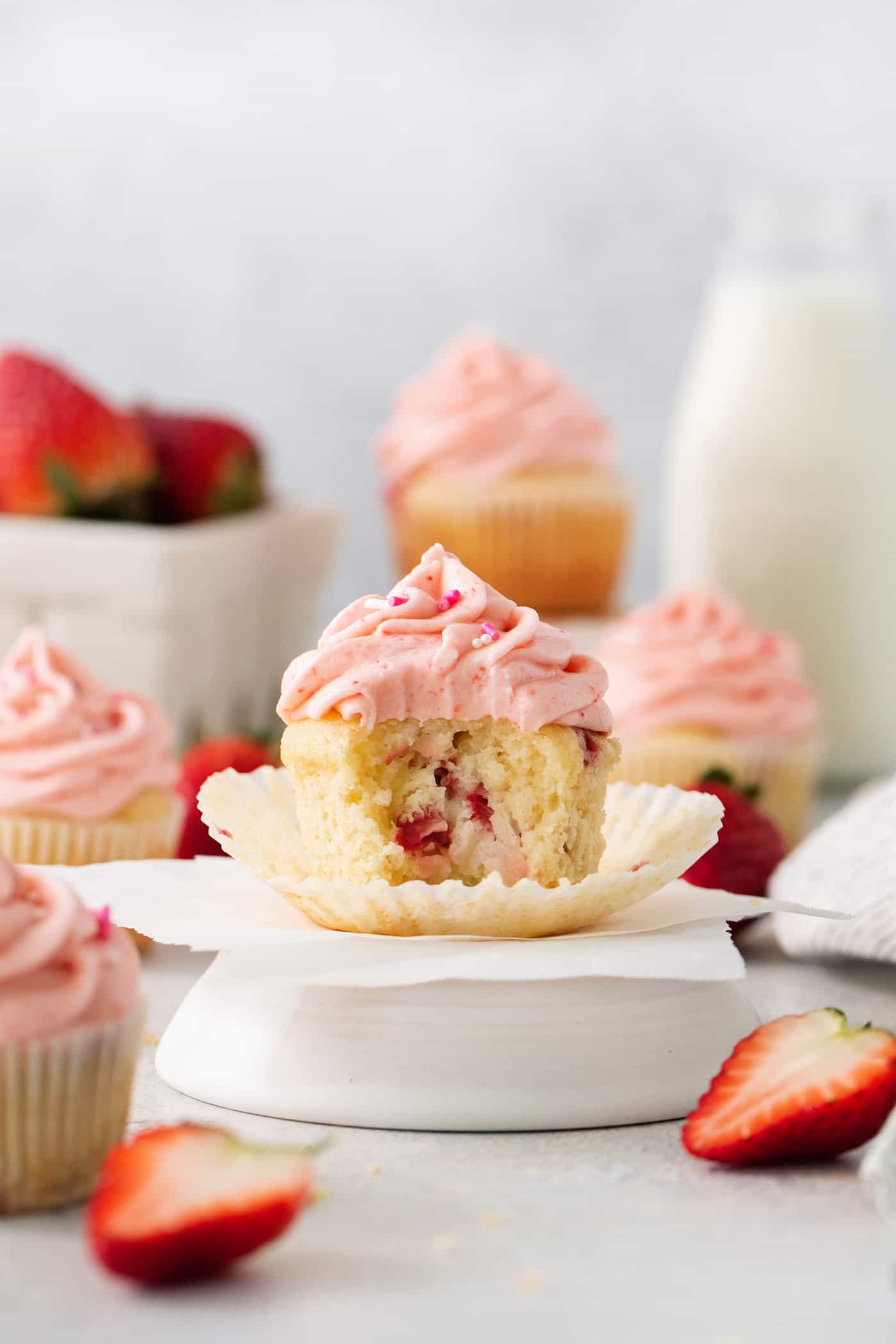 A batch of frosted strawberry cupcakes is shown with one cupcake cut open to show the interior.