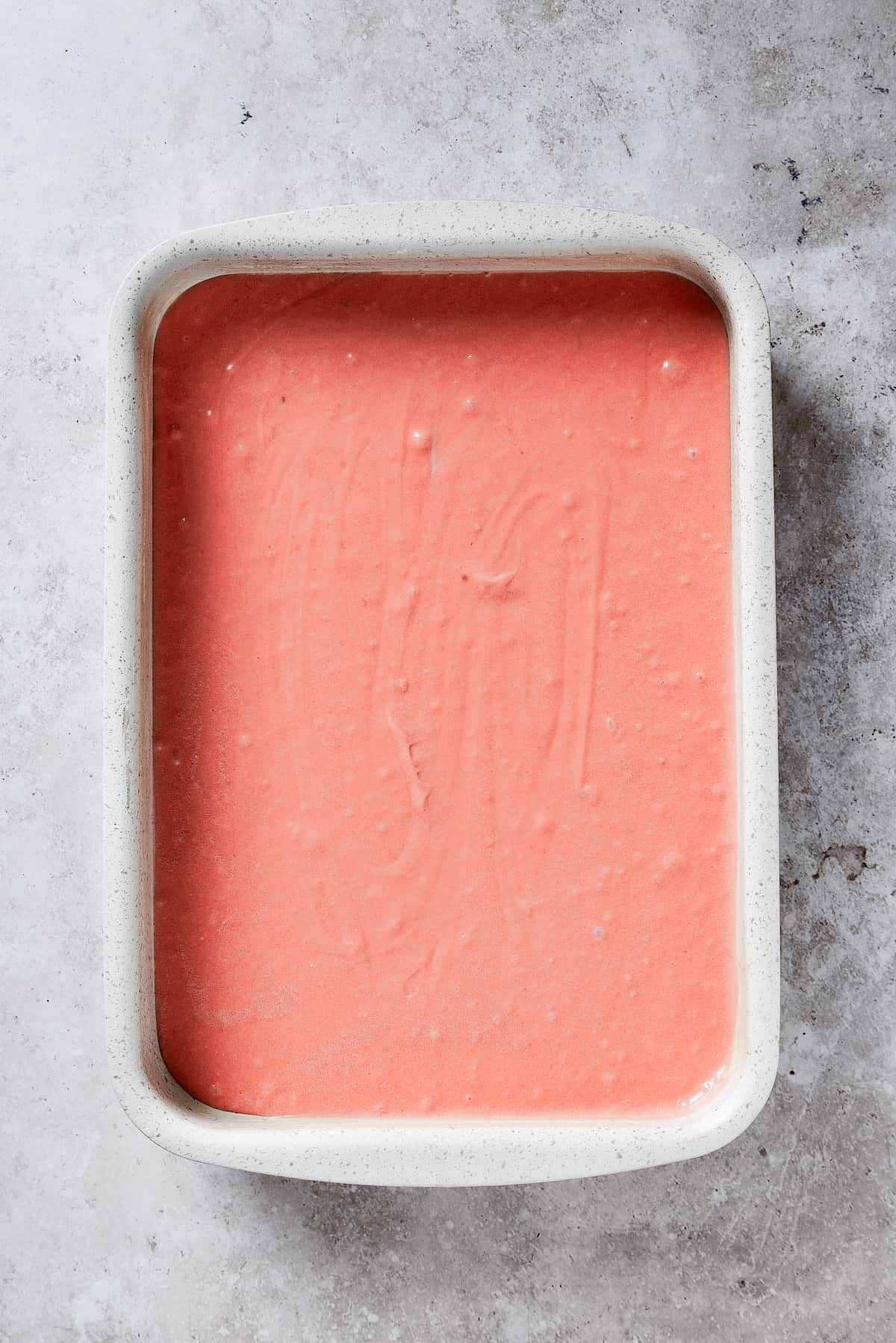 Pink strawberry crunch cake batter is shown in a white pan.