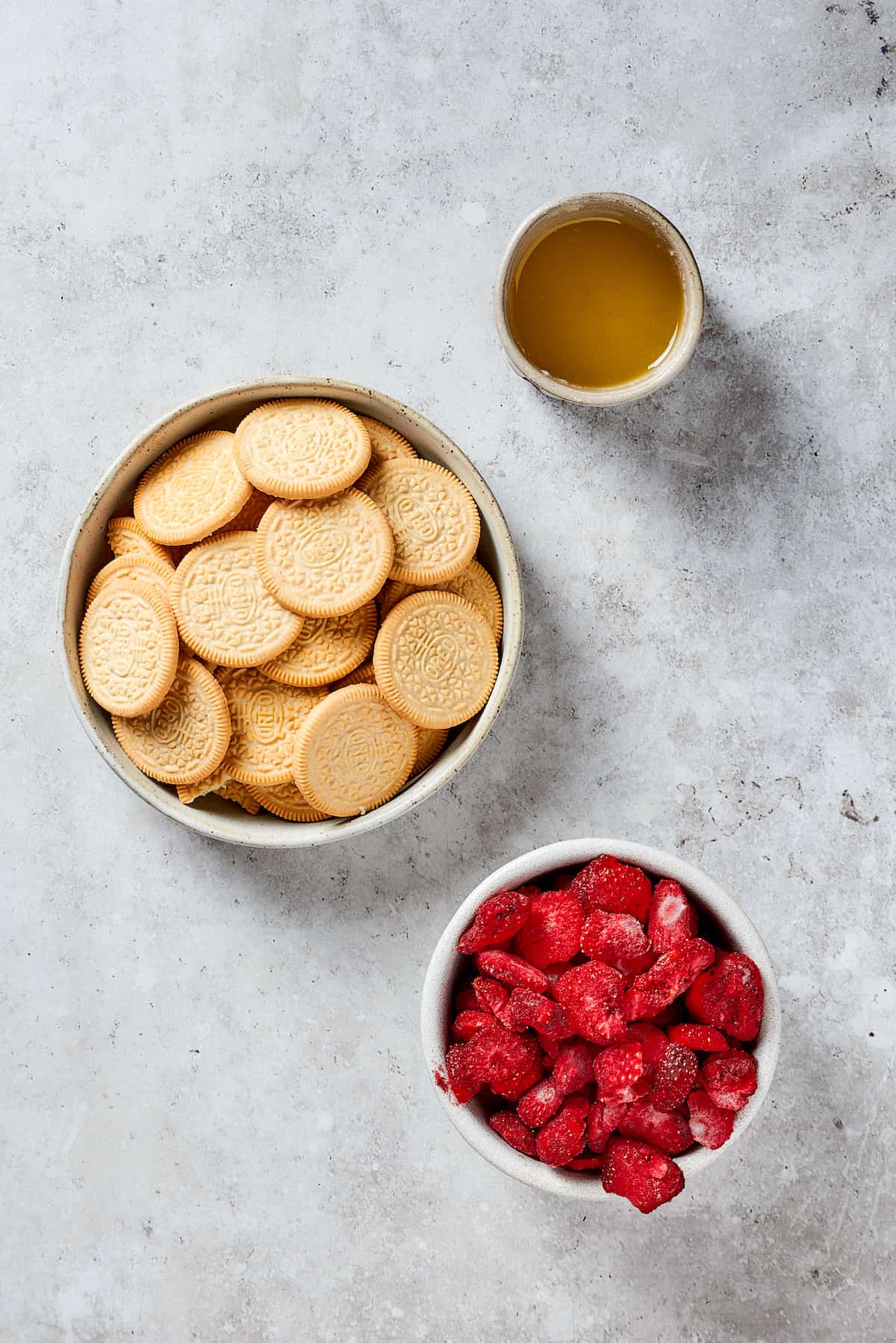 Topping ingredients for strawberry crunch cake are shown including pieces of golden Oreos, freeze-dried strawberries and vanilla.