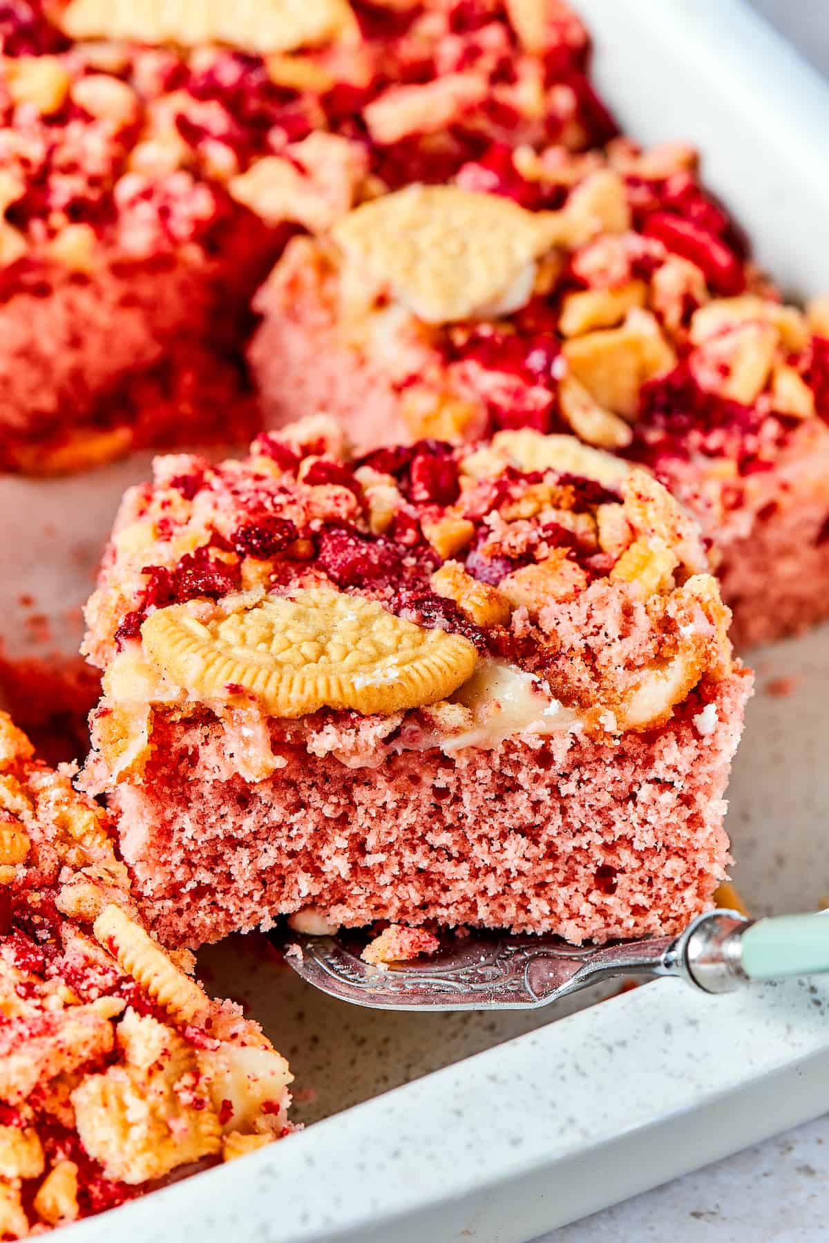 A piece of strawberry crunch cake is lifted out of a pan.